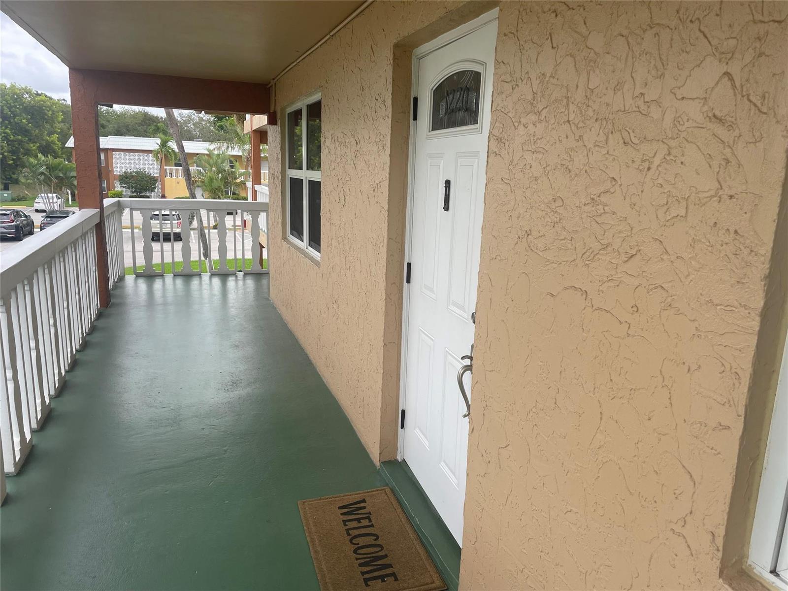 A covered balcony with a green floor and a white door featuring a welcome mat — 9818 Marina Boulevard # 1220, Boca Raton FL 33428, BOCA RATON, FL