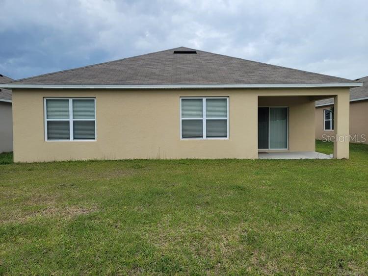 The rear exterior of a tan stucco house features a covered patio and sliding doors — 376 TANGLEWOOD DRIVE, DAVENPORT, FL