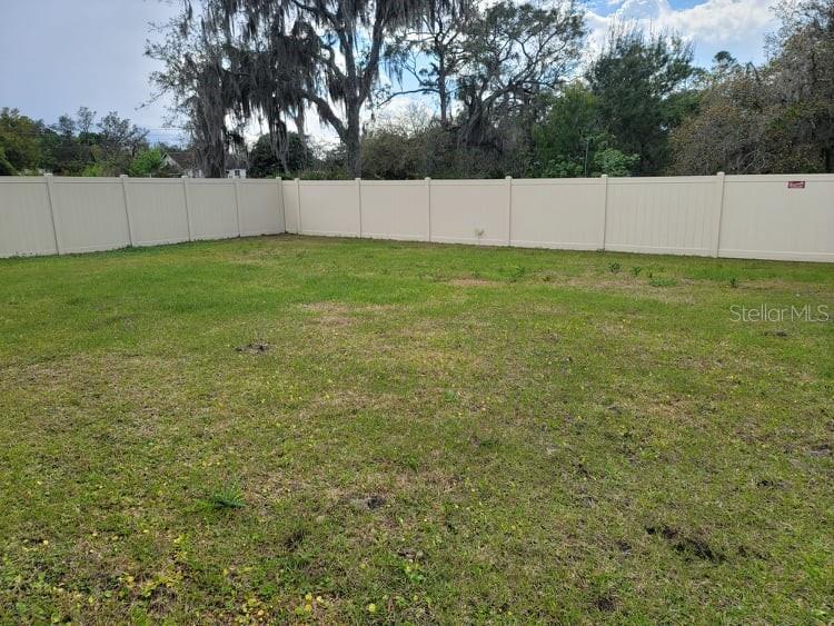 A large, grassy backyard is enclosed by a tall, tan vinyl privacy fence — 376 TANGLEWOOD DRIVE, DAVENPORT, FL