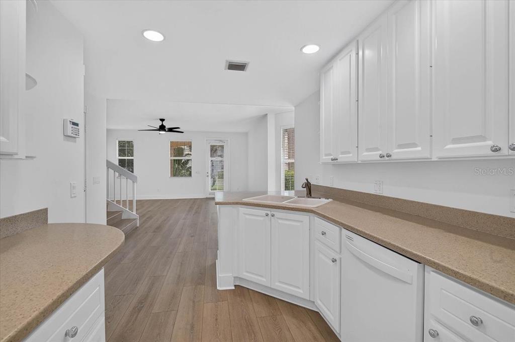 A kitchen with white cabinets and tan countertops overlooks a living area with wood flooring — 5975 GIARDINO LANE, SARASOTA, FL