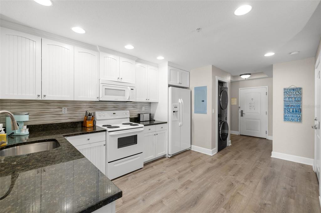 A kitchen features white cabinets, dark granite countertops, stainless steel appliances, and wood-look flooring — 399 2ND STREET UNIT 216, INDIAN ROCKS BEACH, FL