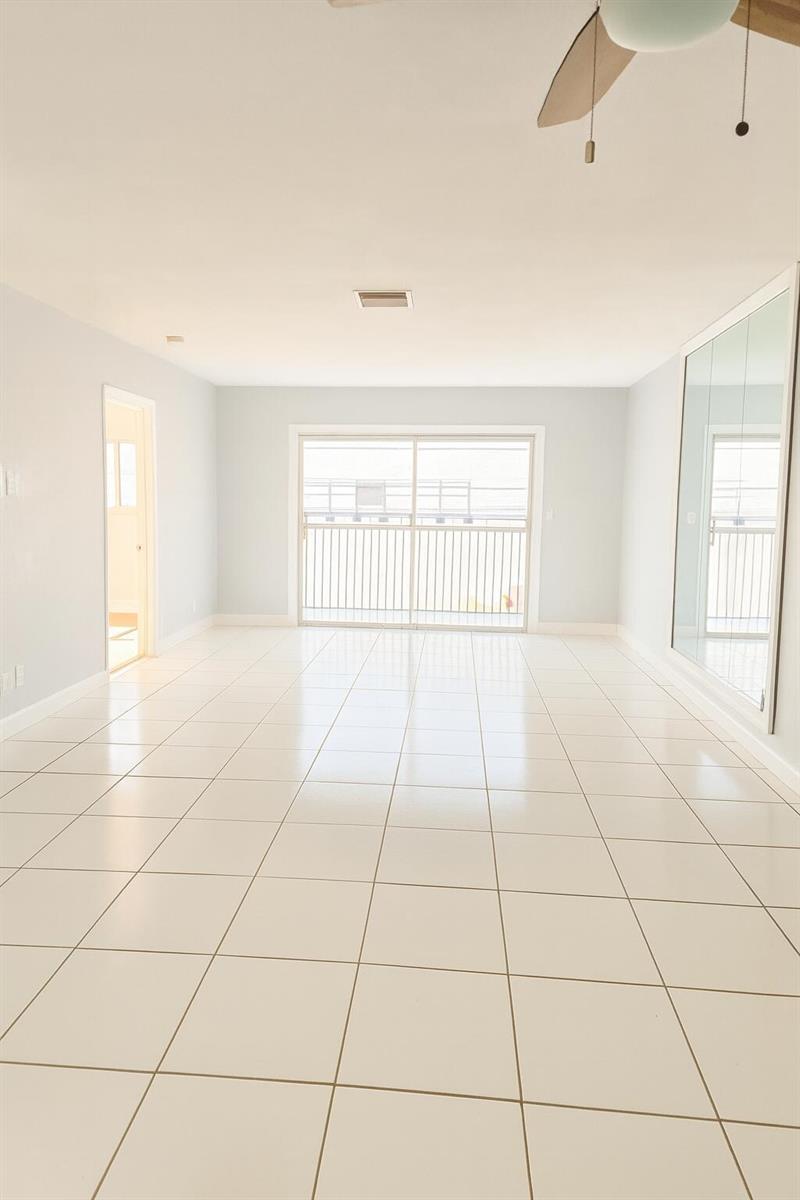 An empty room features white tile flooring, light blue walls, and a sliding glass door — 1001 SE 3rd Street # 3, Deerfield Beach FL 33441, DEERFIELD BEACH, FL