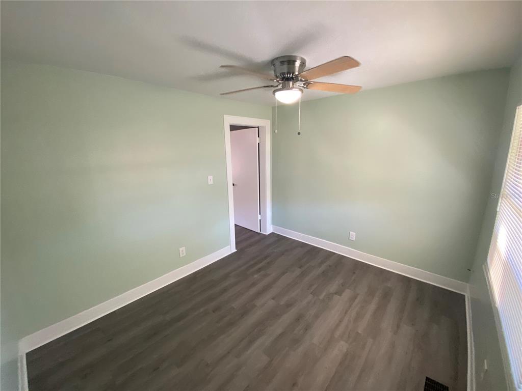 A bedroom with light green walls, wood-look flooring, and a ceiling fan — 227 E BARNES AVENUE, EUSTIS, FL