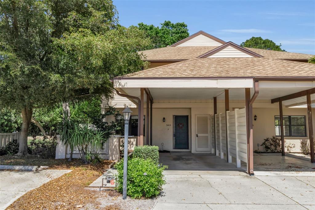 A two-story townhouse exterior features a covered carport, a front door, and a large tree — 3415 51ST AVENUE CIRCLE W UNIT 206, BRADENTON, FL
