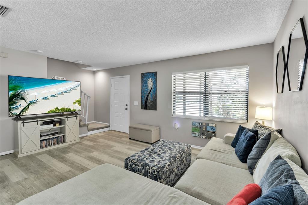 A living room features a large television on a white console, sectional sofa, and stairs — 3415 51ST AVENUE CIRCLE W UNIT 206, BRADENTON, FL