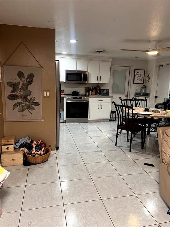 A kitchen with white cabinets, stainless steel appliances, and tile flooring opens to a dining area — 210 WALNUT AVENUE NW, PORT CHARLOTTE, FL