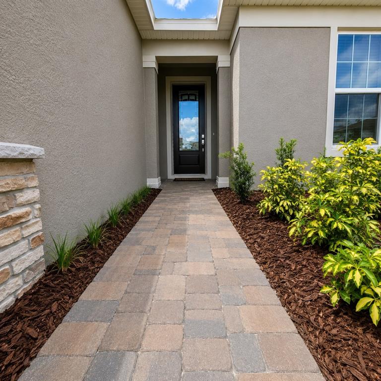 A paved walkway leads to a dark front door framed by stucco walls and landscaping — 17391 SAW PALMETTO AVENUE, CLERMONT, FL