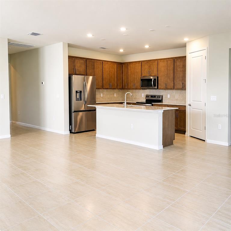 A kitchen features brown cabinetry, stainless steel appliances, a white island, and light tile flooring — 17391 SAW PALMETTO AVENUE, CLERMONT, FL