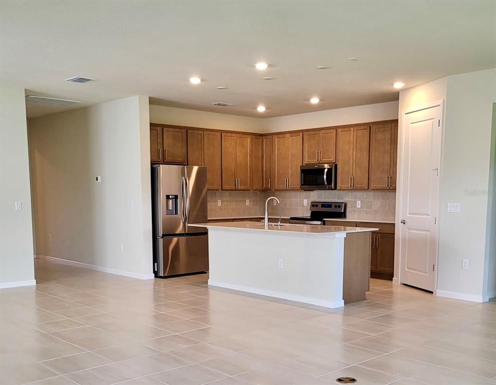 A kitchen features wood cabinets, stainless steel appliances, a center island, and tile flooring — 17391 SAW PALMETTO AVENUE, CLERMONT, FL