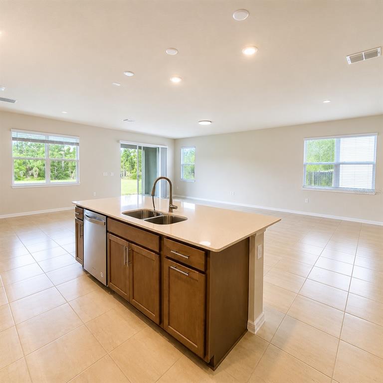 A kitchen island with a sink and dishwasher sits in an open-concept room with tile floors — 17391 SAW PALMETTO AVENUE, CLERMONT, FL