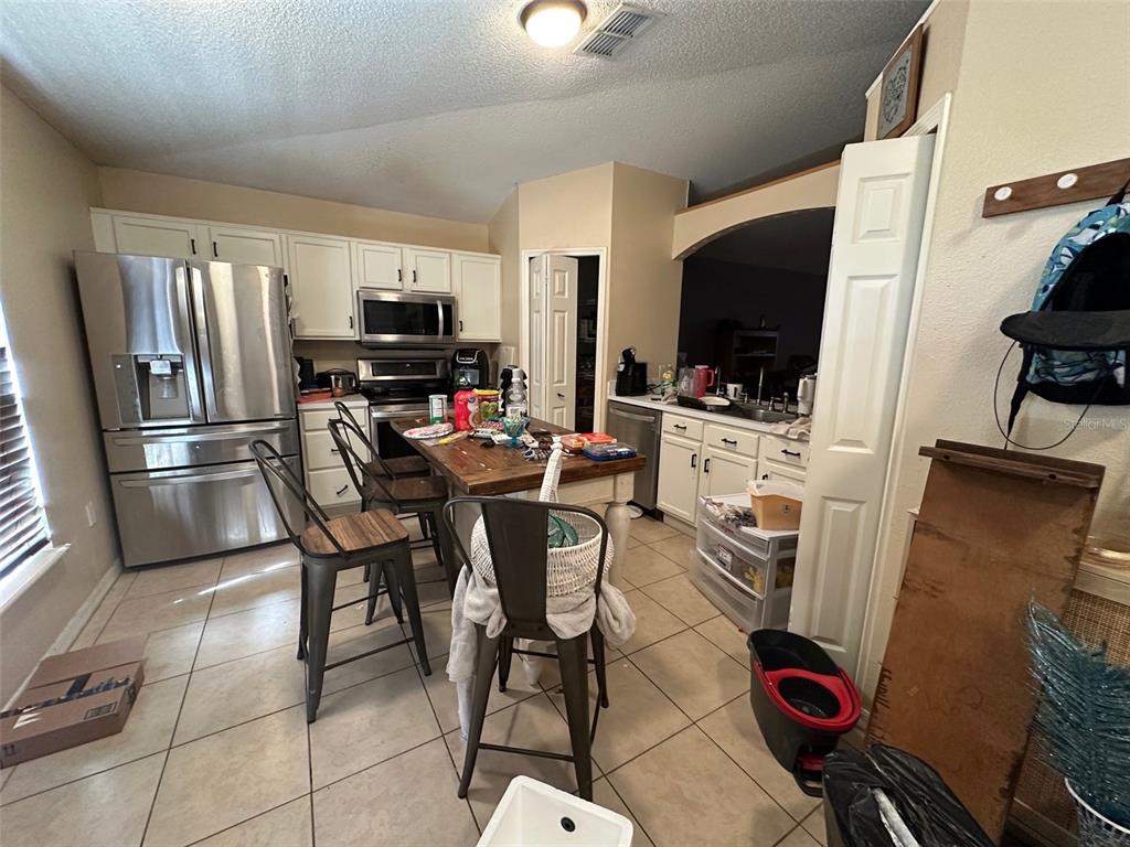 A kitchen features stainless steel appliances, white cabinets, a wooden island, and tile flooring — 1909 LAKEVIEW PLACE, KISSIMMEE, FL