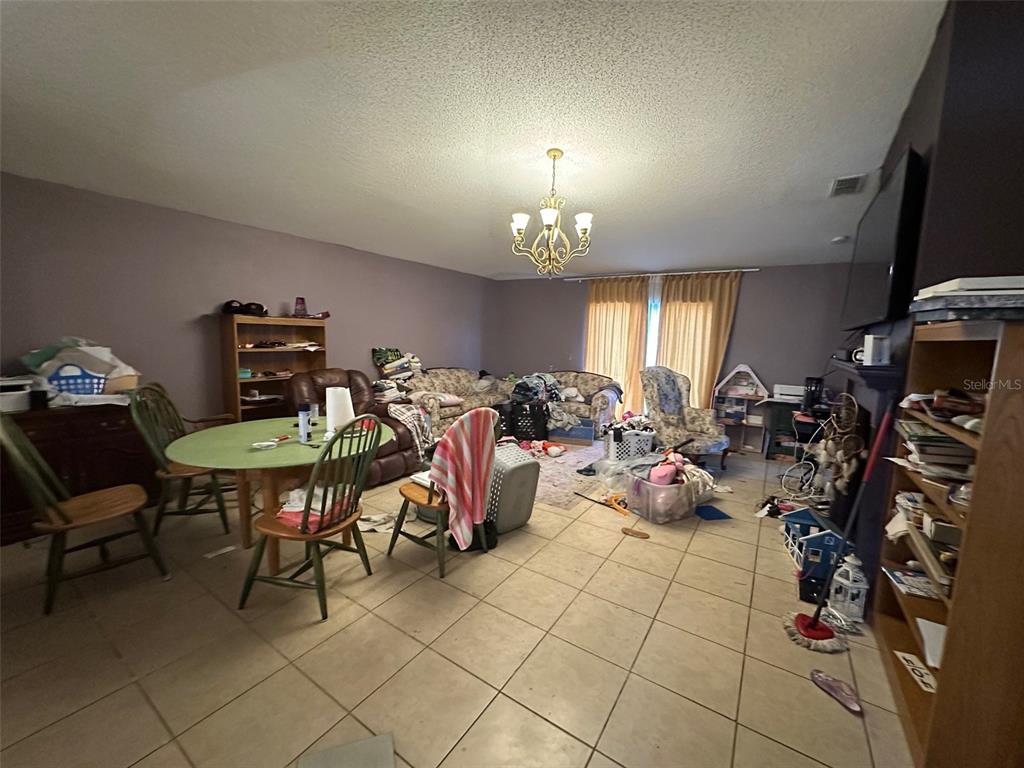 A living and dining area with tile flooring, a chandelier, and cluttered furniture — 1909 LAKEVIEW PLACE, KISSIMMEE, FL