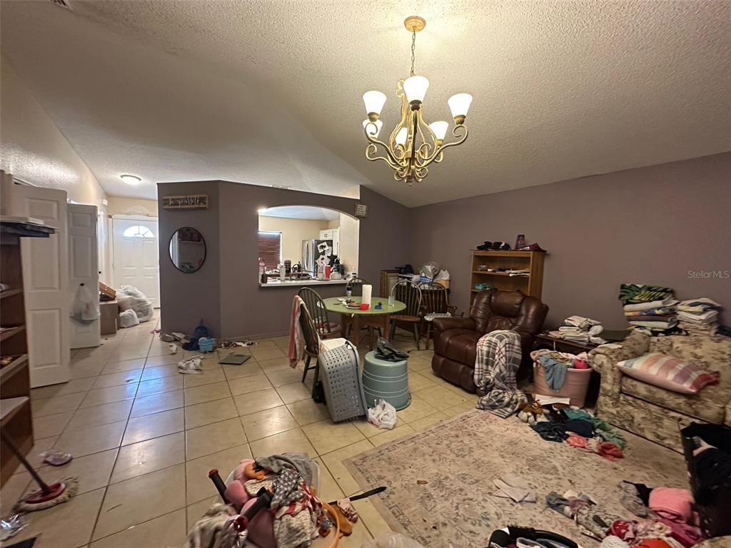 A living room with tile flooring, a chandelier, and a dining area visible through an opening — 1909 LAKEVIEW PLACE, KISSIMMEE, FL