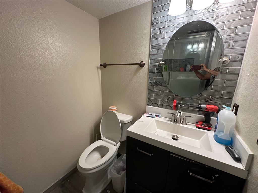 A bathroom features a white toilet, a dark vanity with a sink, and gray tiled backsplash — 1909 LAKEVIEW PLACE, KISSIMMEE, FL