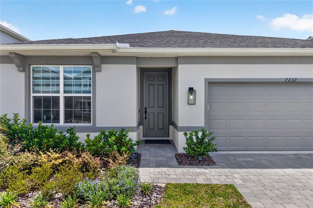 The exterior of a single-story house features a gray front door, garage, and landscaped yard — 7239 IVY TENDRIL AVENUE, ORLANDO, FL
