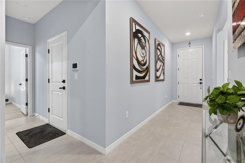A bright entryway features light blue walls, tile flooring, two framed abstract paintings, and doors — 7239 IVY TENDRIL AVENUE, ORLANDO, FL