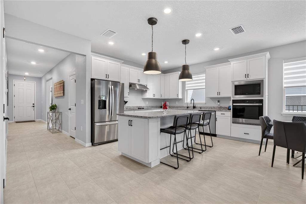 A modern kitchen features white cabinetry, granite countertops, a central island, and stainless steel appliances — 7239 IVY TENDRIL AVENUE, ORLANDO, FL