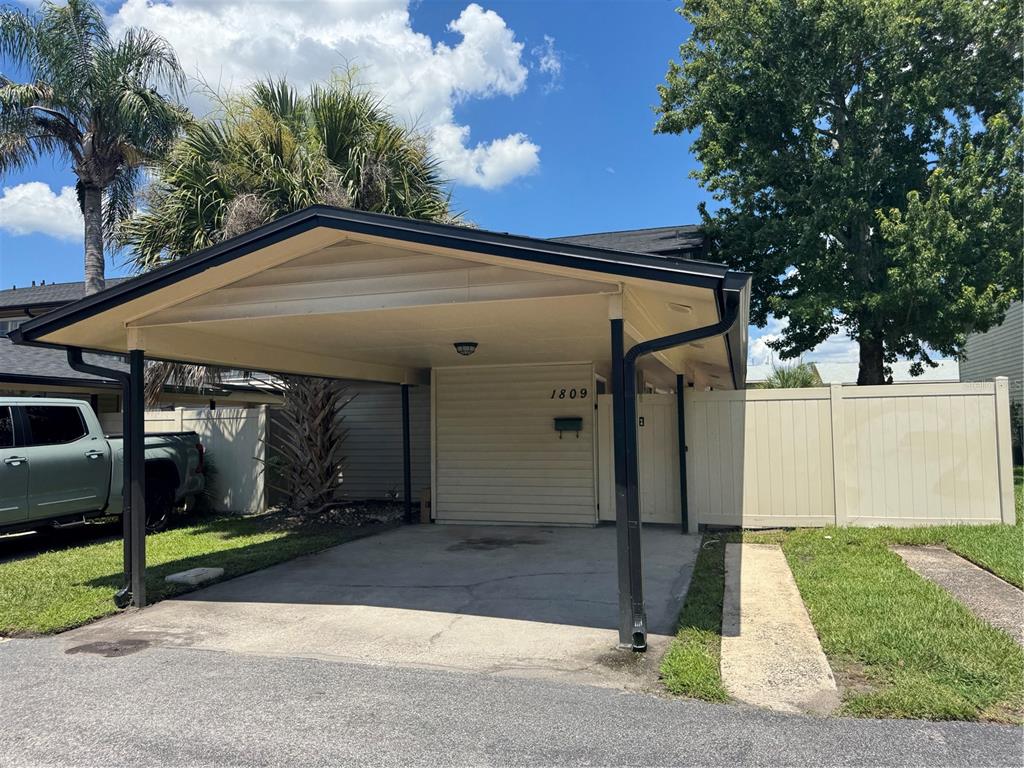 A carport with a concrete driveway sits in front of a house with beige siding — 1809 TOWNHALL LANE UNIT 1809, ORLANDO, FL