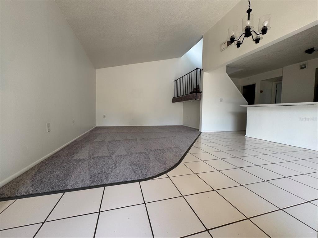 A living room features a raised carpeted area, tiled flooring, and a staircase with railing — 1809 TOWNHALL LANE UNIT 1809, ORLANDO, FL