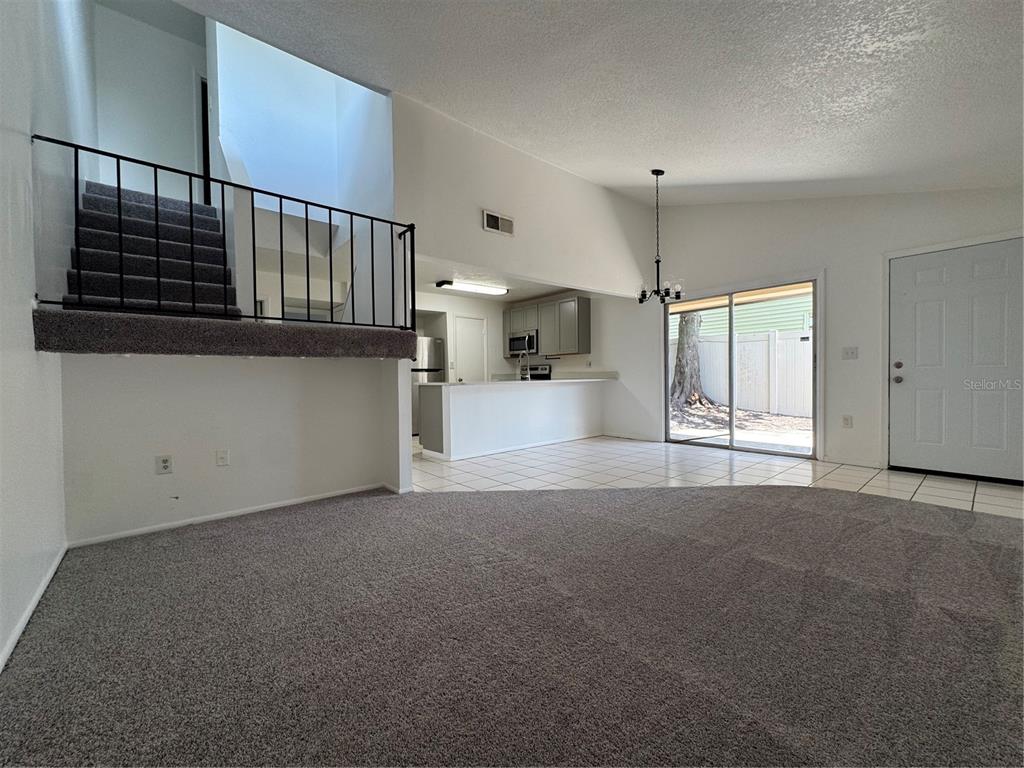 A living room with gray carpet, a staircase with black railings, and an adjacent kitchen — 1809 TOWNHALL LANE UNIT 1809, ORLANDO, FL
