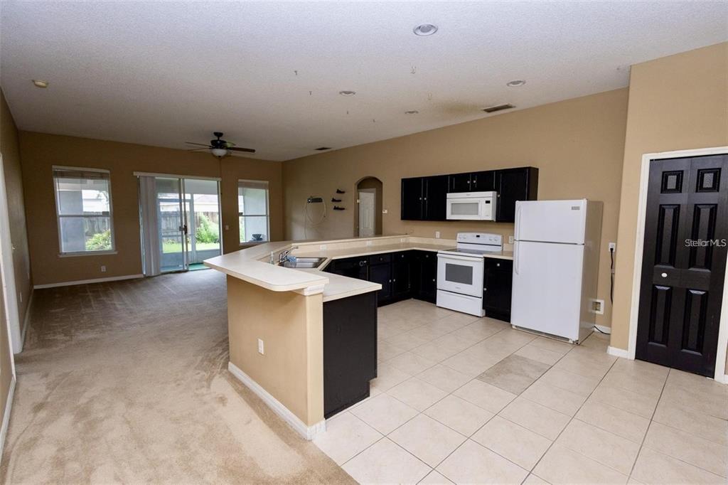 A kitchen with black cabinets and white appliances opens to a carpeted living area — 818 CARROUSEL LANE, KISSIMMEE, FL