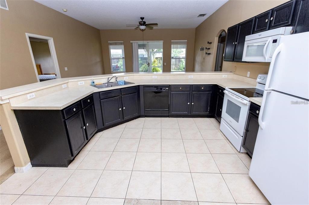 A kitchen features black cabinets, white appliances, a light-colored countertop, and tiled flooring — 818 CARROUSEL LANE, KISSIMMEE, FL