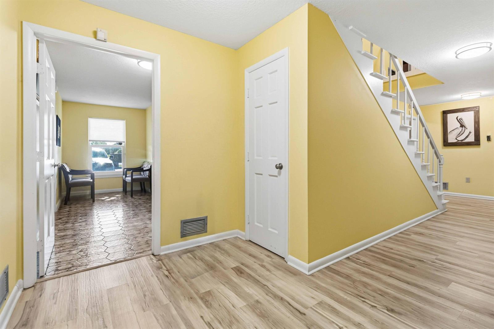 A yellow-walled entryway features light wood-look flooring, a staircase, and a doorway to a room — 111 Scott Street, Melbourne FL 32901, MELBOURNE, FL