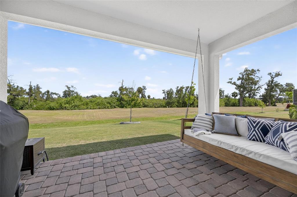 A covered patio features a hanging daybed, brick pavers, and a view of a grassy field — 1019 SIGNET DRIVE, APOLLO BEACH, FL