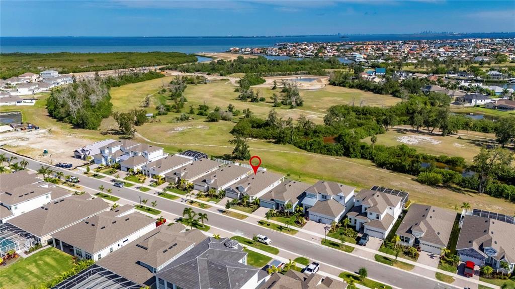 An aerial view shows a suburban neighborhood with houses bordering a large, undeveloped grassy area — 1019 SIGNET DRIVE, APOLLO BEACH, FL