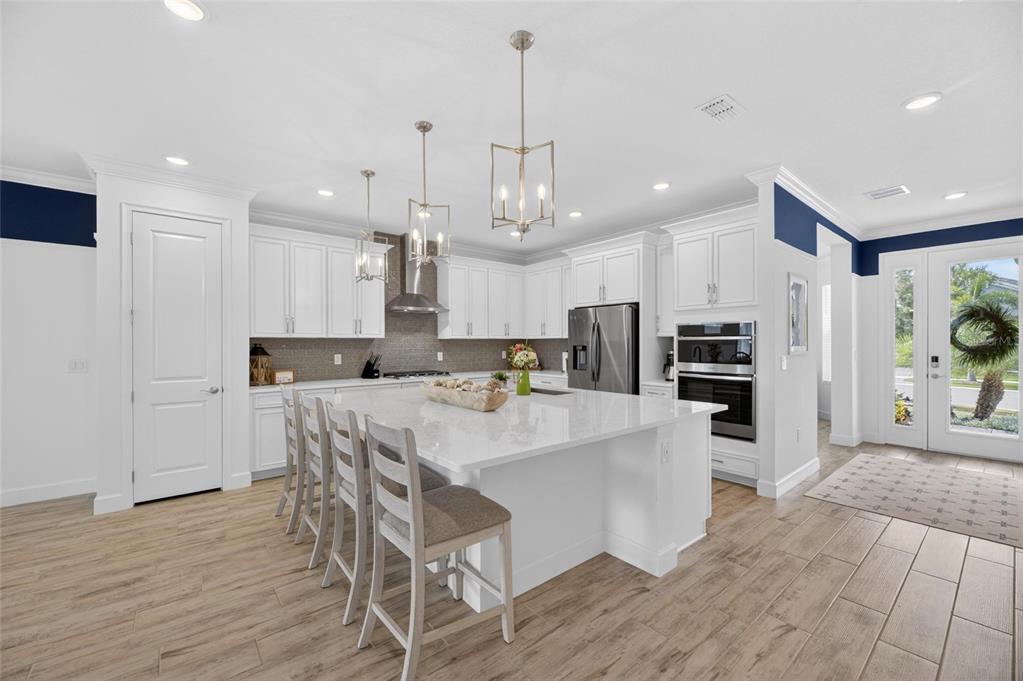 A modern white kitchen features a large quartz island, stainless steel appliances, and wood-look flooring — 1019 SIGNET DRIVE, APOLLO BEACH, FL