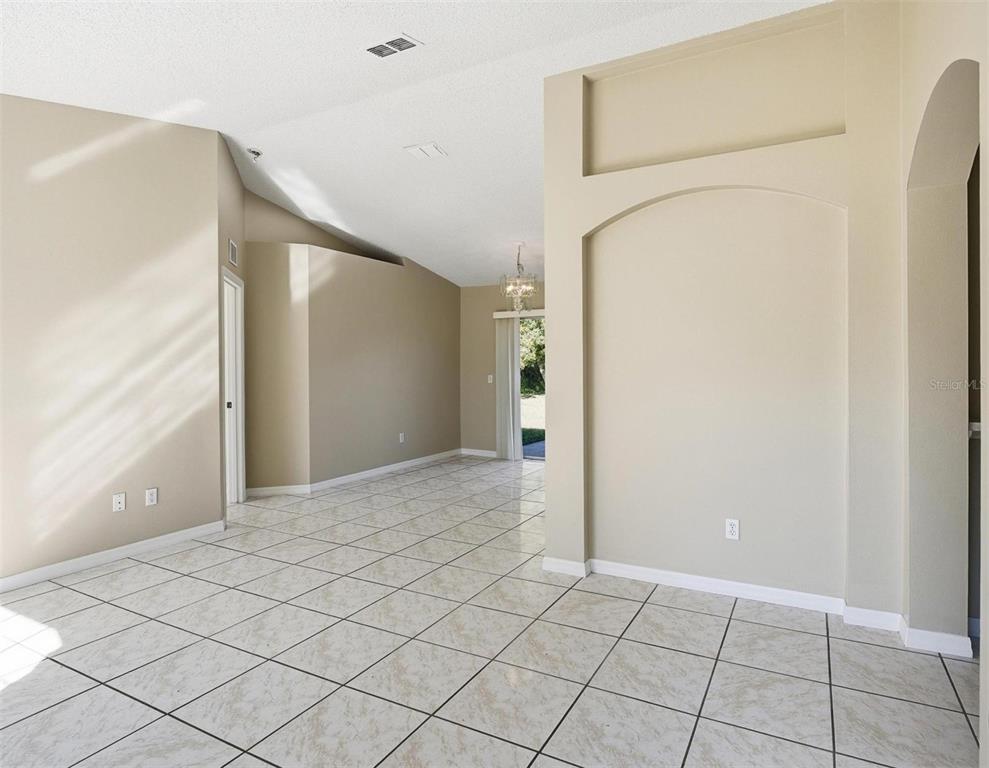 An empty room with beige walls, vaulted ceilings, and light-colored tile flooring — 106 LA MANCHA DRIVE, PALM COAST, FL