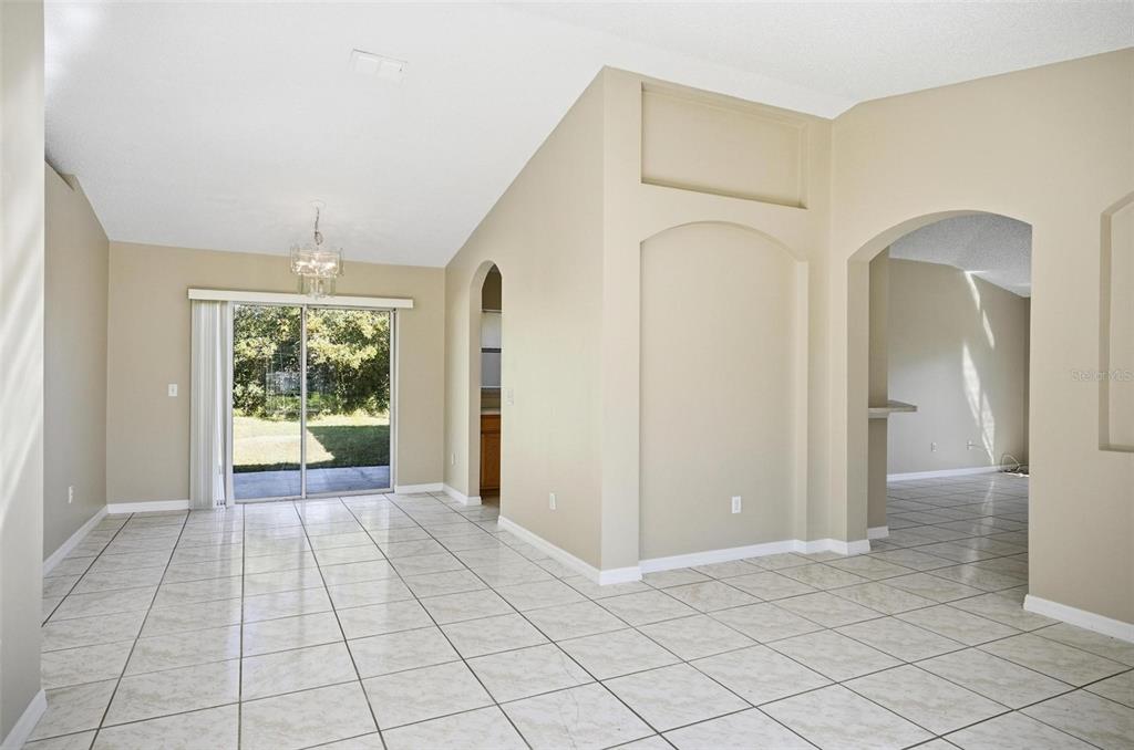 A bright, tiled living area features a vaulted ceiling, arched doorways, and a sliding glass door — 106 LA MANCHA DRIVE, PALM COAST, FL