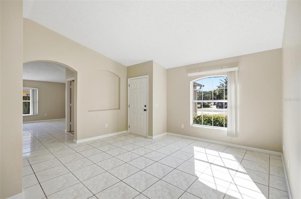 An empty room with beige walls, white tile flooring, an arched doorway, and a window — 106 LA MANCHA DRIVE, PALM COAST, FL