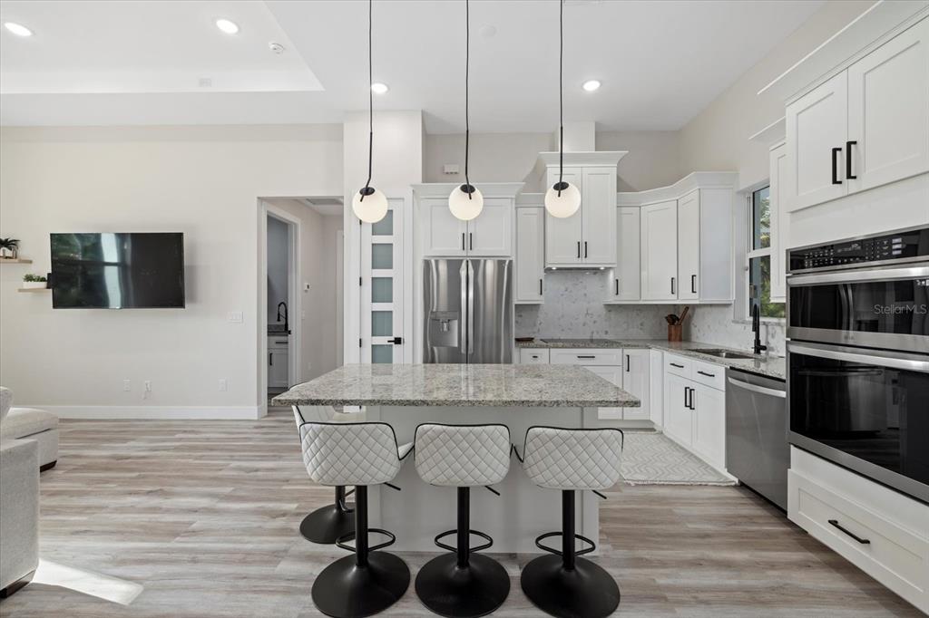 A modern kitchen features white cabinets, granite countertops, a central island, and three pendant lights — 2938 JASON STREET, NORTH PORT, FL