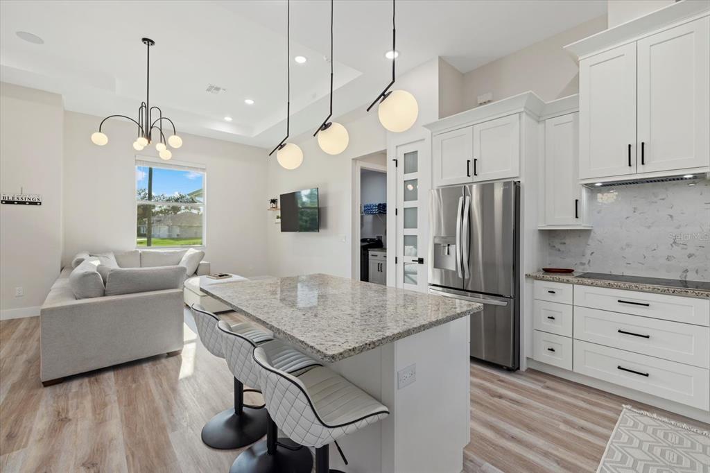 A modern kitchen features a granite island, white cabinetry, stainless appliances, and an adjacent living area — 2938 JASON STREET, NORTH PORT, FL