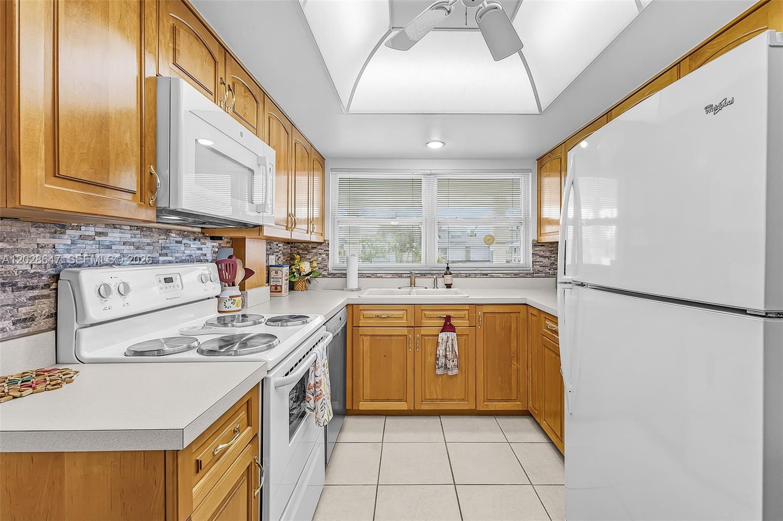 A galley kitchen features wood cabinets, white appliances, a tiled backsplash, and a ceiling fan — 8 watercolor way, Naples FL 34113, NAPLES, FL