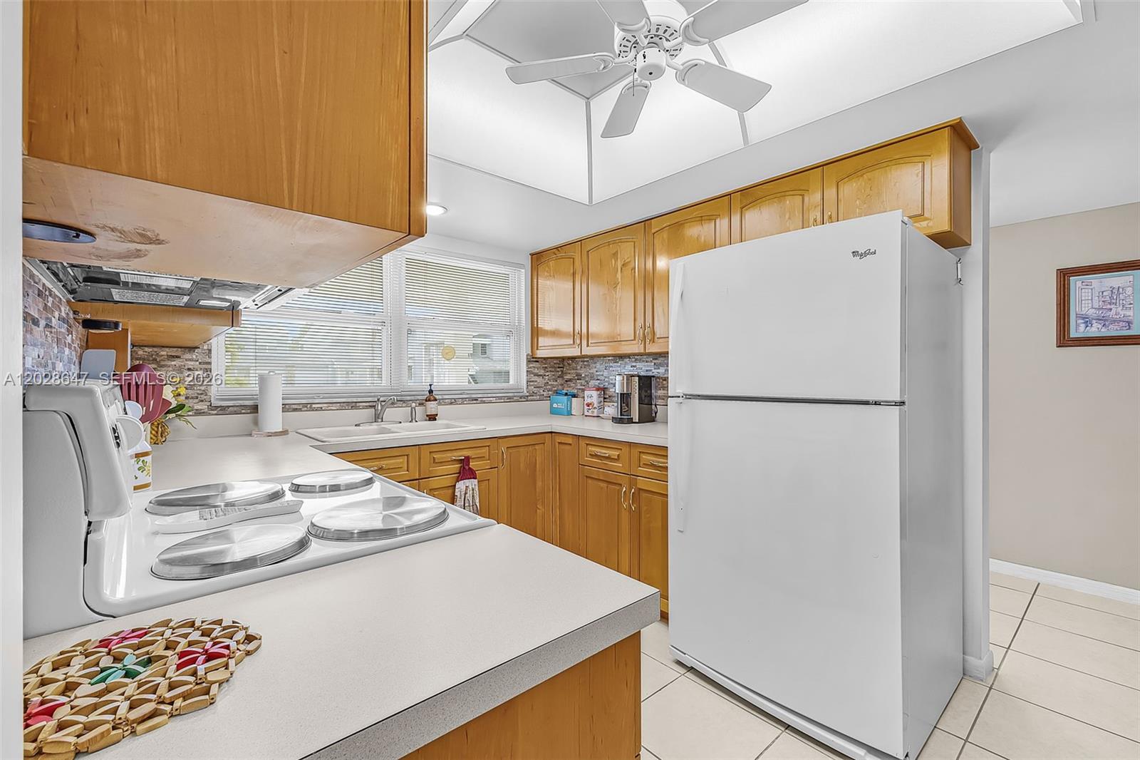 A kitchen features light wood cabinets, white appliances, a ceiling fan, and tiled flooring — 8 watercolor way, Naples FL 34113, NAPLES, FL
