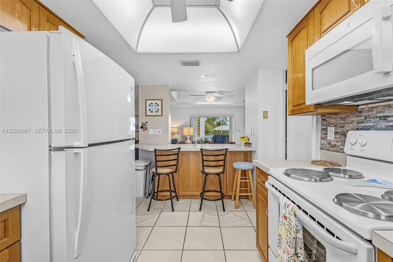 A kitchen with white appliances, wooden cabinets, and a breakfast bar overlooking a living area — 8 watercolor way, Naples FL 34113, NAPLES, FL