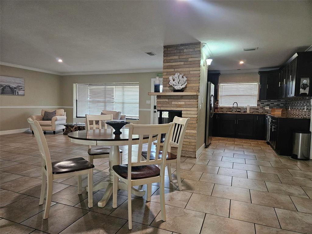 An open-concept room features a dining set, a stone fireplace, and a dark-cabinet kitchen — 1417 27TH STREET W, BRADENTON, FL