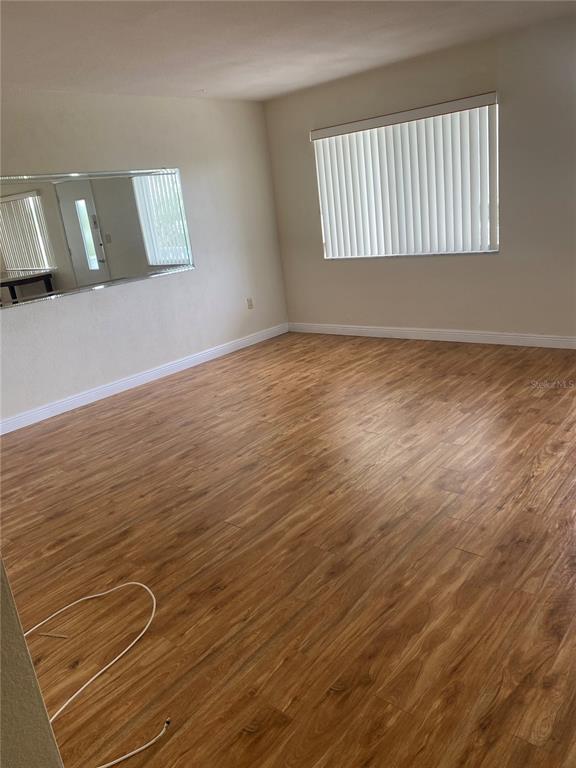 An empty room features wood-look flooring, a large wall mirror, and a window with blinds — 11224 82ND AVENUE UNIT 301, SEMINOLE, FL