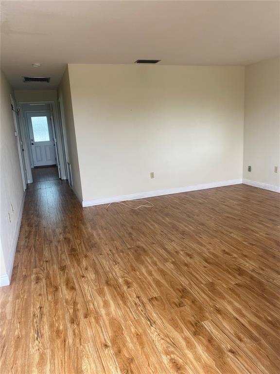 An empty room with light-colored walls and wood-look flooring leads to a hallway and door — 11224 82ND AVENUE UNIT 301, SEMINOLE, FL