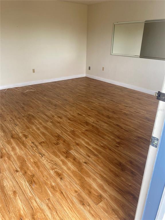 An empty room features wood-look laminate flooring, beige walls, and a wall-mounted mirror — 11224 82ND AVENUE UNIT 301, SEMINOLE, FL