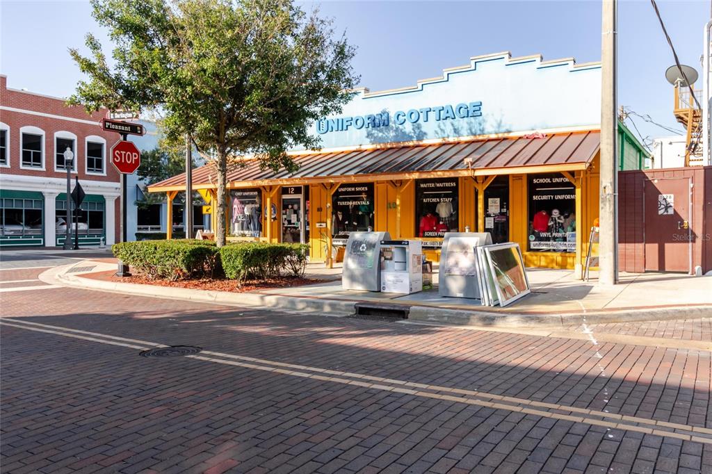 A street-level view of a yellow commercial building named Uniform Cottage on a brick road — 12 E DARLINGTON AVENUE, KISSIMMEE, FL