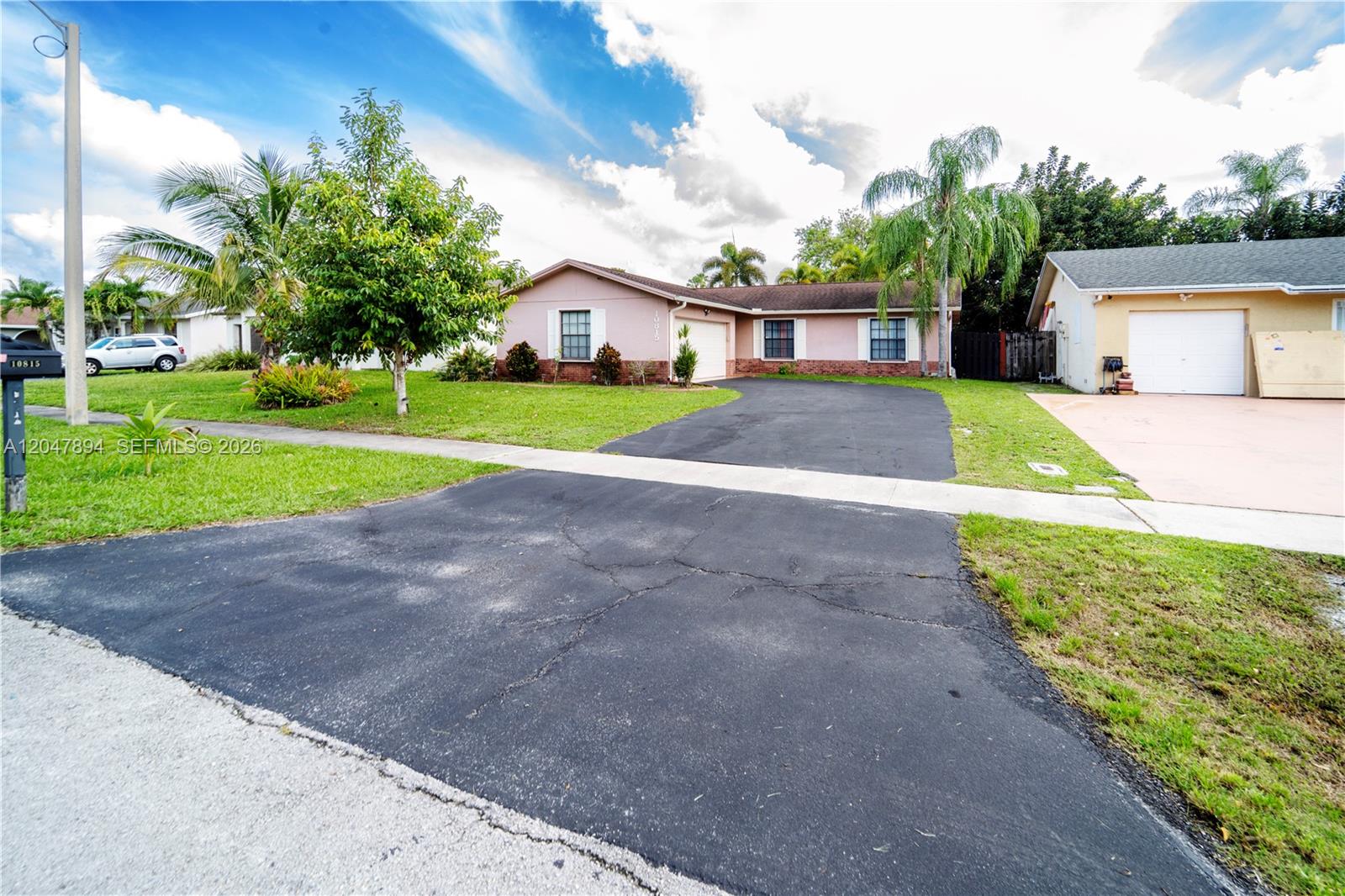 A single-story pink house features a black asphalt driveway and a green front lawn — 10815 NW 26th St, Sunrise FL 33322, SUNRISE, FL