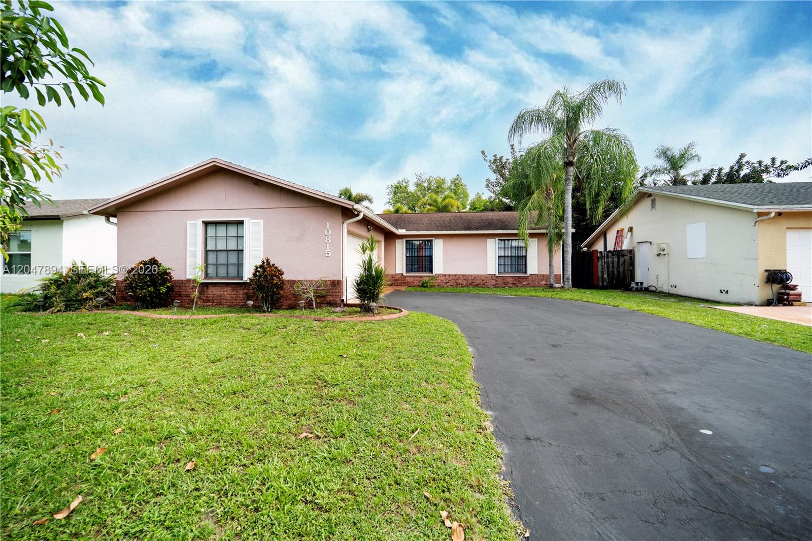 A single-story house with a pink stucco exterior, brick accents, and a paved driveway — 10815 NW 26th St, Sunrise FL 33322, SUNRISE, FL