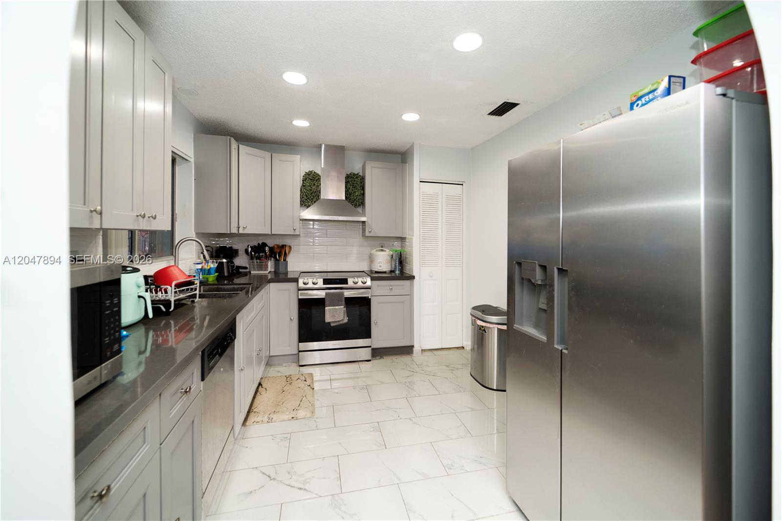 A modern kitchen features gray cabinets, stainless steel appliances, and white marble-look tile flooring — 10815 NW 26th St, Sunrise FL 33322, SUNRISE, FL
