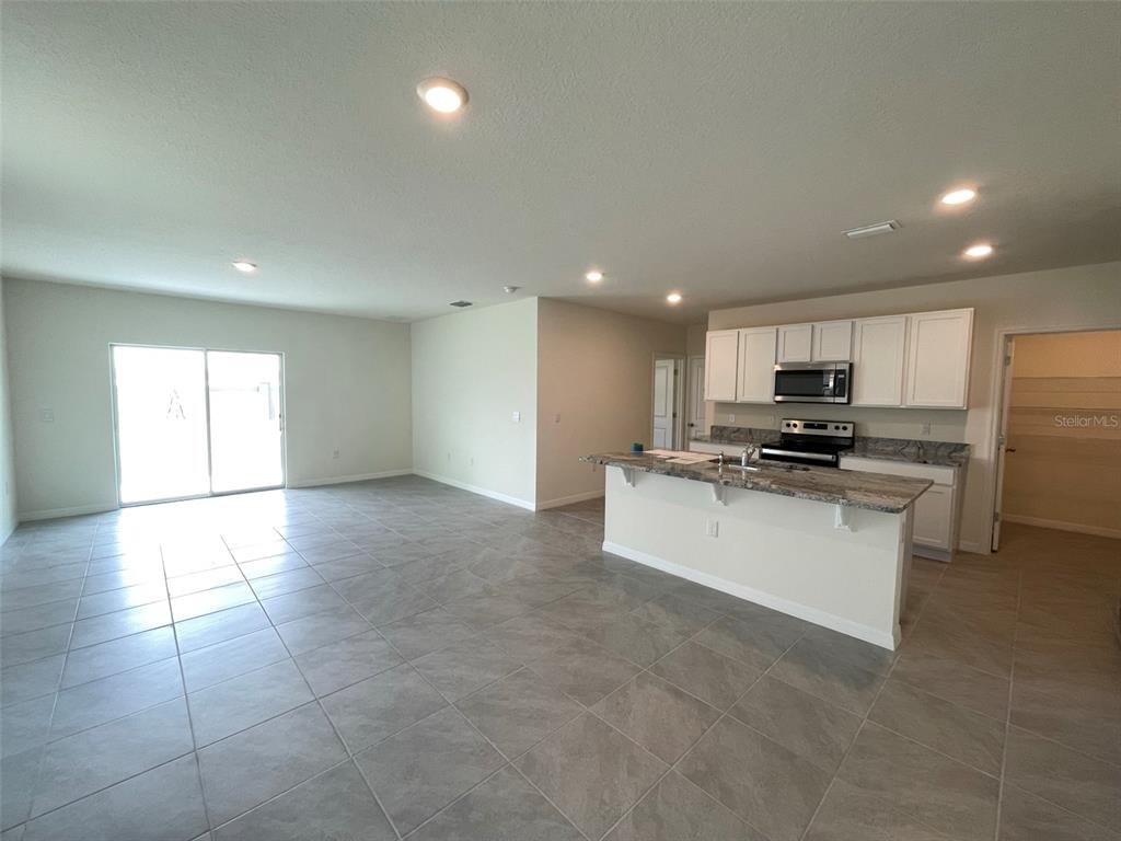 An open-concept kitchen with granite countertops and tile flooring overlooks a spacious living area — 30859 PENNY SURF LOOP, WESLEY CHAPEL, FL