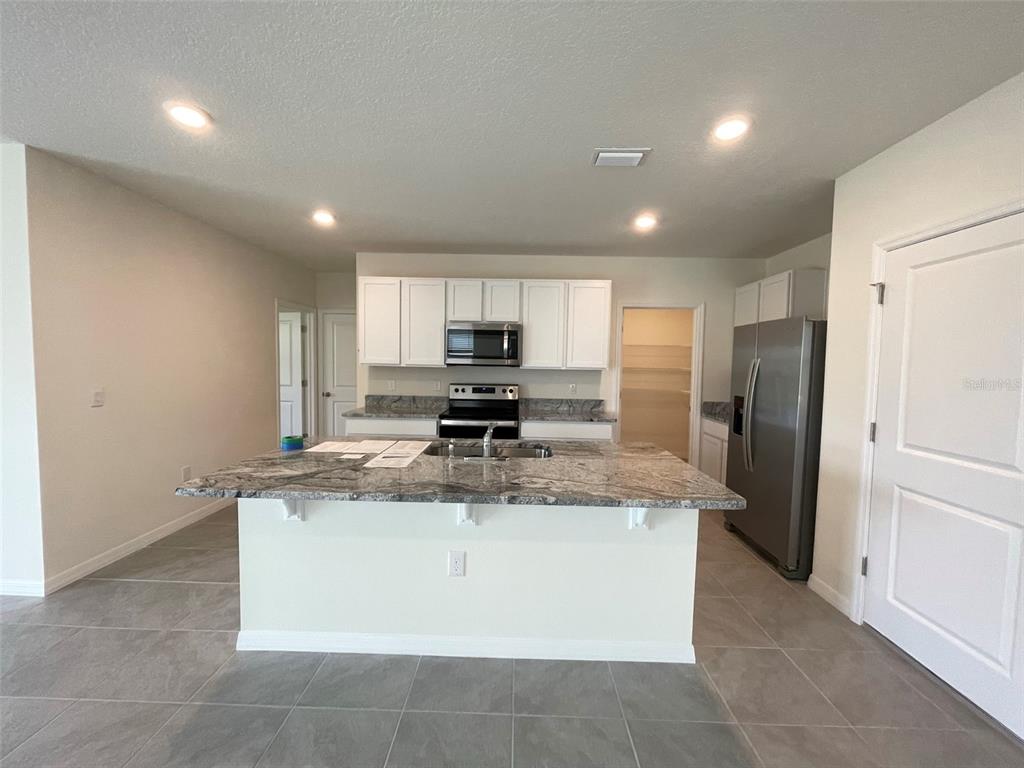 A kitchen features white cabinets, stainless steel appliances, a granite island, and gray tile flooring — 30859 PENNY SURF LOOP, WESLEY CHAPEL, FL