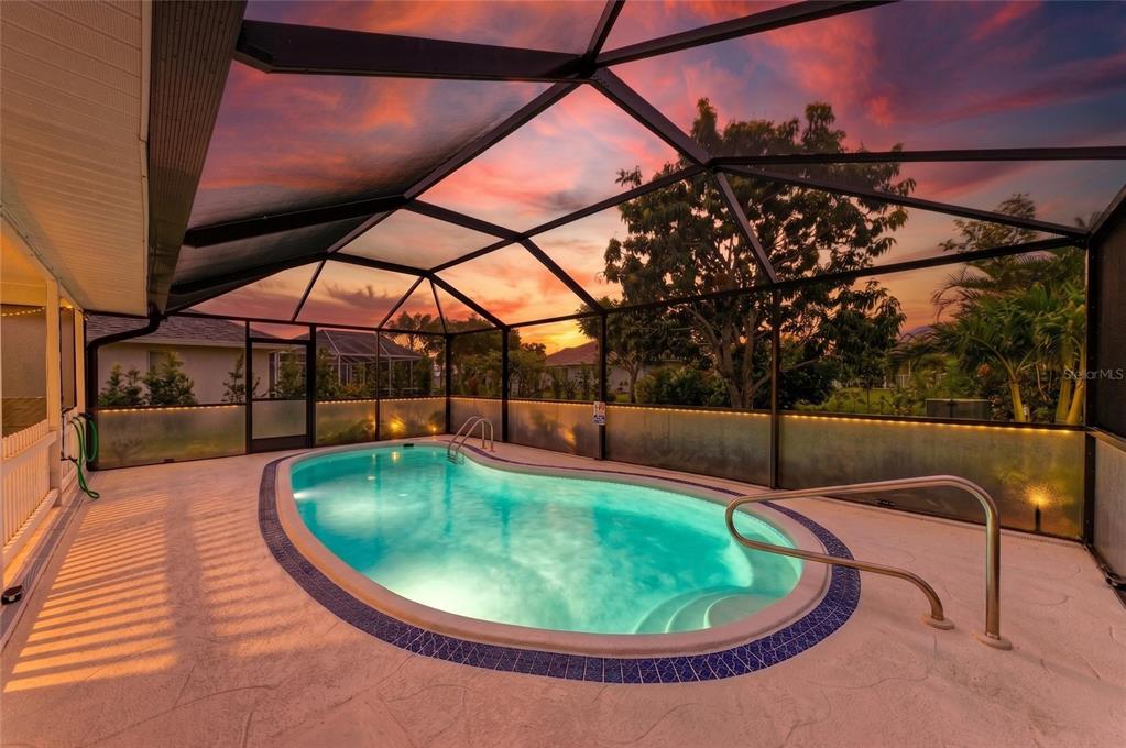 An outdoor swimming pool is enclosed by a screened lanai at sunset — 405 BAYSIDE LANE, NOKOMIS, FL