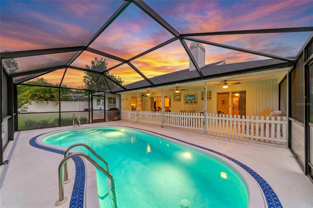 A swimming pool sits inside a screened-in lanai with a white fence and house exterior — 405 BAYSIDE LANE, NOKOMIS, FL